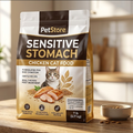 A bag of PetStore Sensitive Stomach Chicken Cat Food stands on a wooden table in a softly lit kitchen setting, with a small bowl of cat food beside it.